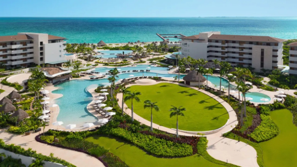 Aerial view of Dreams Playa Mujeres family resort with pools, palm-lined lawn, and Caribbean beach in the background